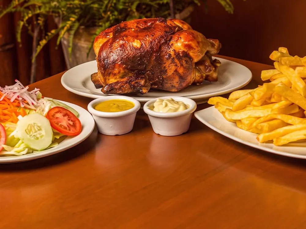 Pollo a la brasa entero con papas fritas, ensalada y cremas sobre una mesa de madera